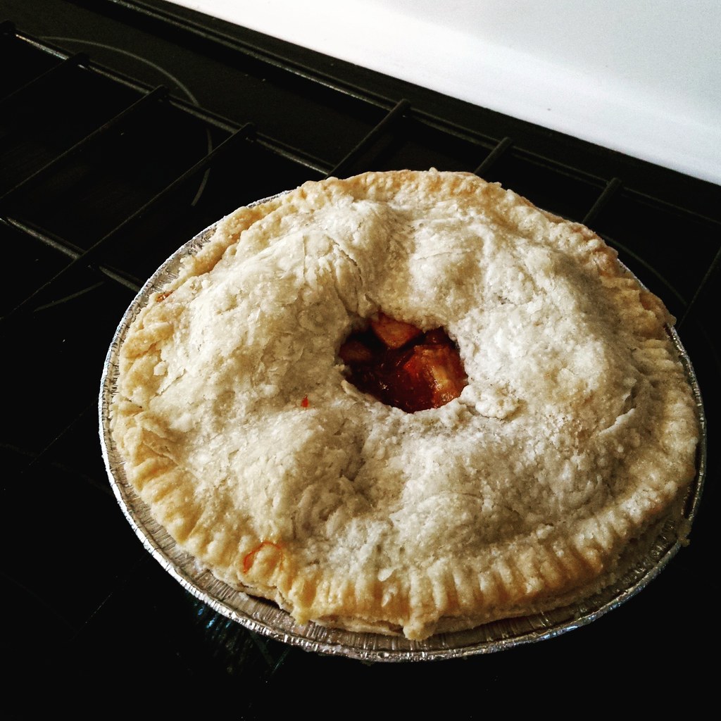 Single serve round apple pie, with pale crust and cut out circle in the middle showing apple chunks. Background is a black stove top.